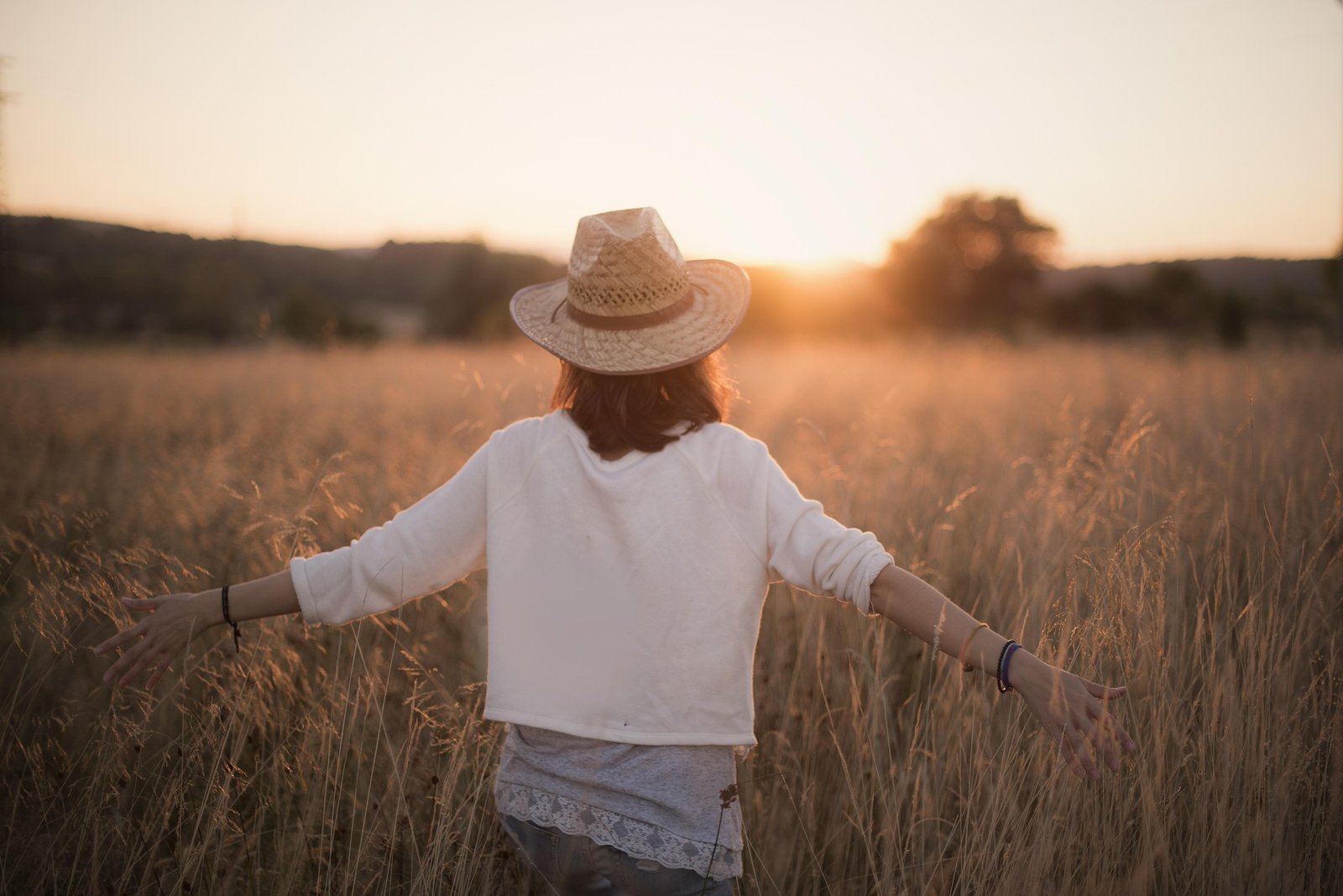 Woman walking through a wheat field at sunset